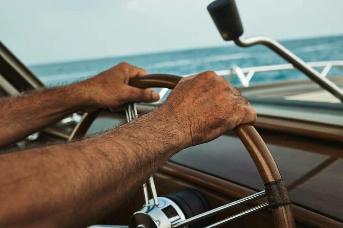 Mani di un comandante sul timone di uno yacht a motore, con il mare all’orizzonte