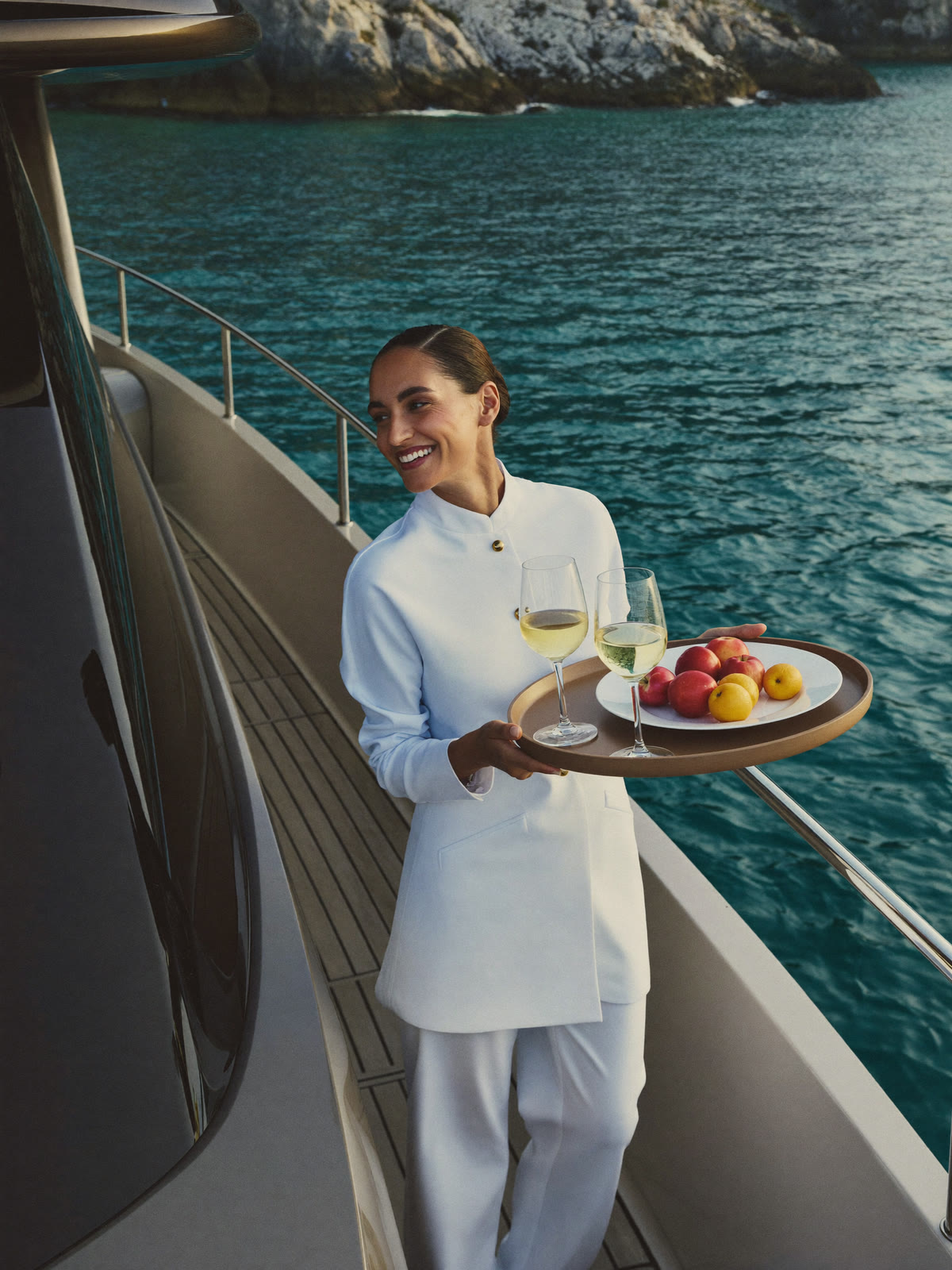 Hostess che serve un aperitivo sul ponte di poppa di uno yacht all’ancora
