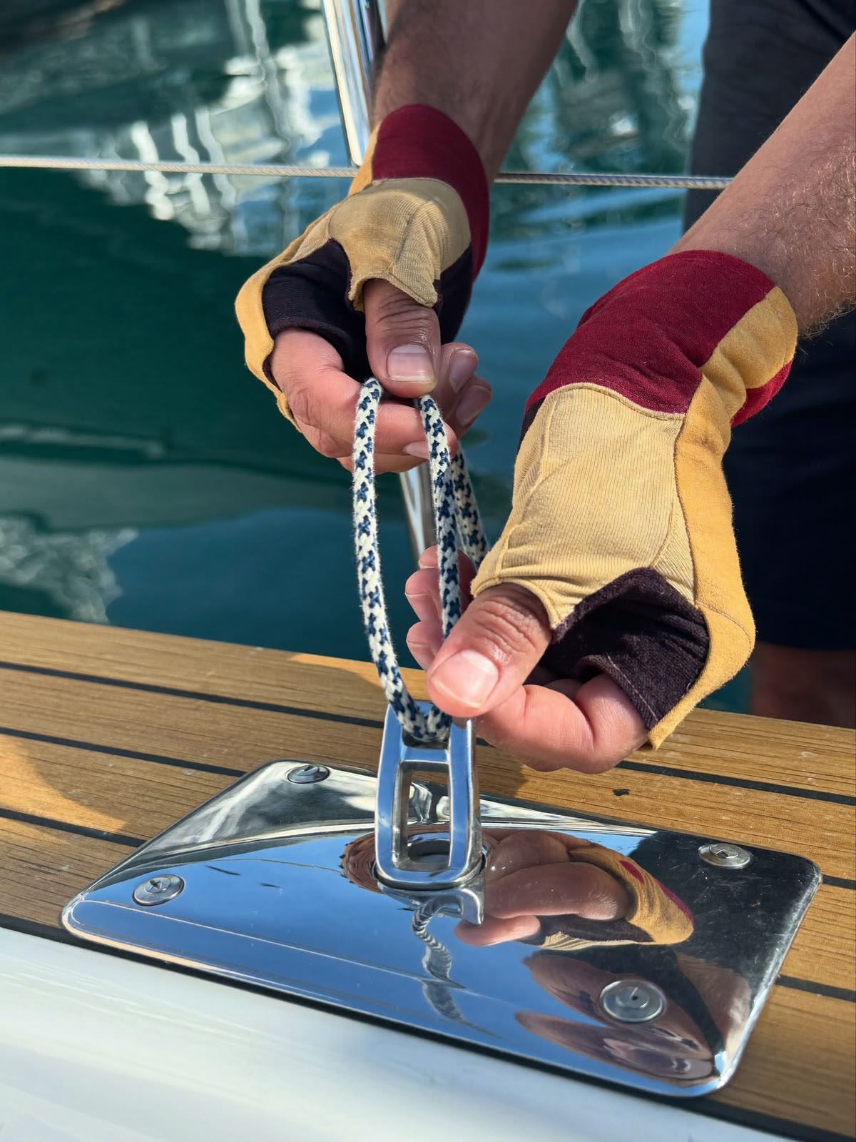 Mani di un marinaio che danno volta a una cima su una bitta in acciaio